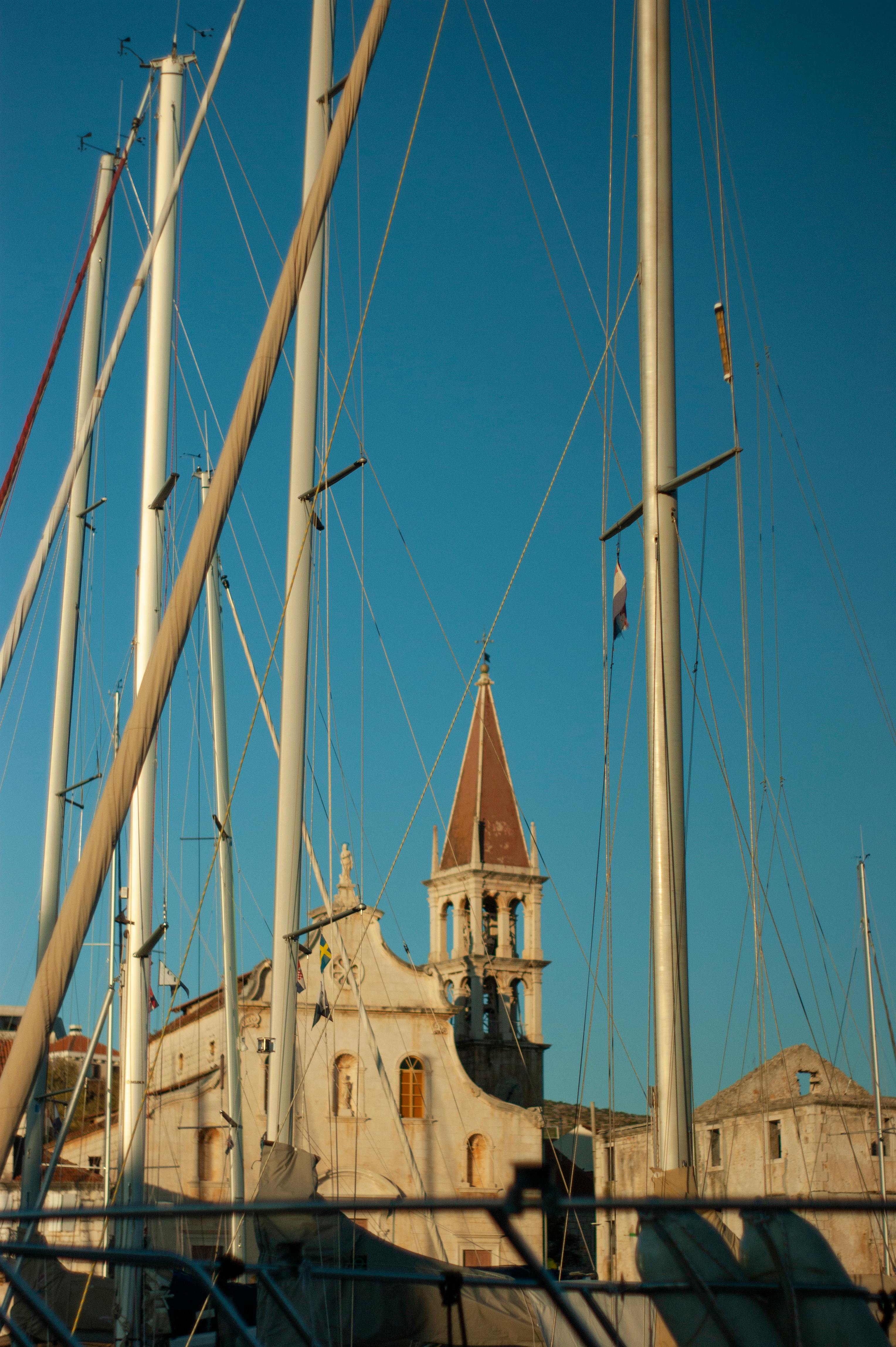 Stunning view of a church tower framed by yacht masts against a clear blue sky in Croatia.