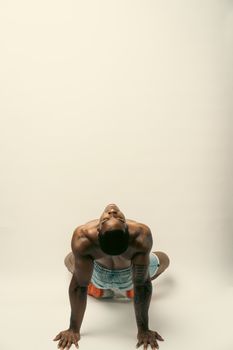 A topless black man in a bending pose captured in a studio, showcasing strong muscle definition and a serene expression.