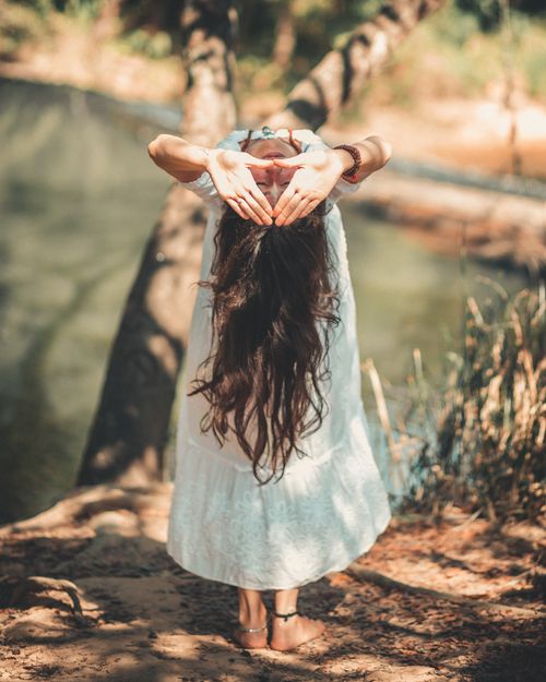Free A woman with long hair performing a yoga pose by a tranquil river in a sunny outdoor setting. Stock Photo
