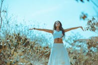 阳光明媚的田野里，一个穿着白色连衣裙的女人正享受着自由与自然