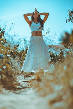 A woman in a white outfit meditating outdoors, embodying relaxation and tranquility.