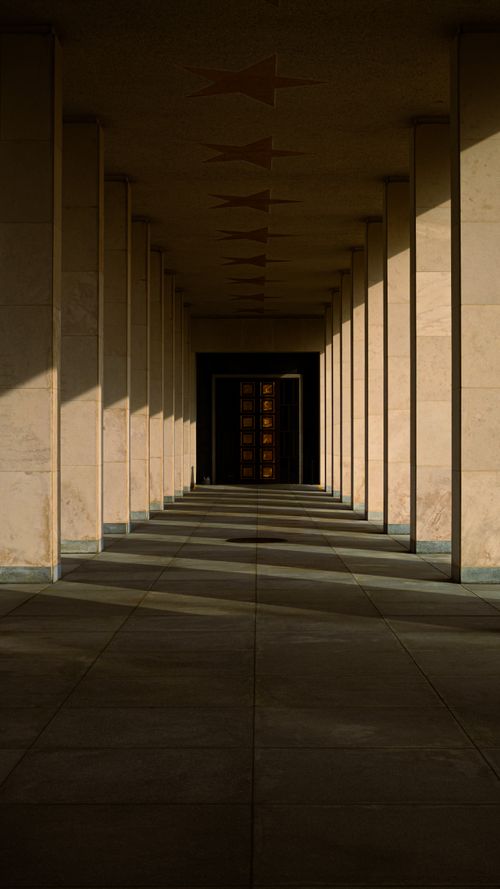 Free A beautiful symmetrical hallway in Belgium with shadows cast by columns, creating an elegant architectural scene. Stock Photo