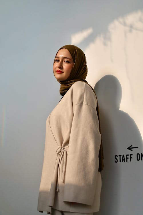 Young Woman in an Elegant Outfit and Hijab Posing in Sunlight against a White Wall 