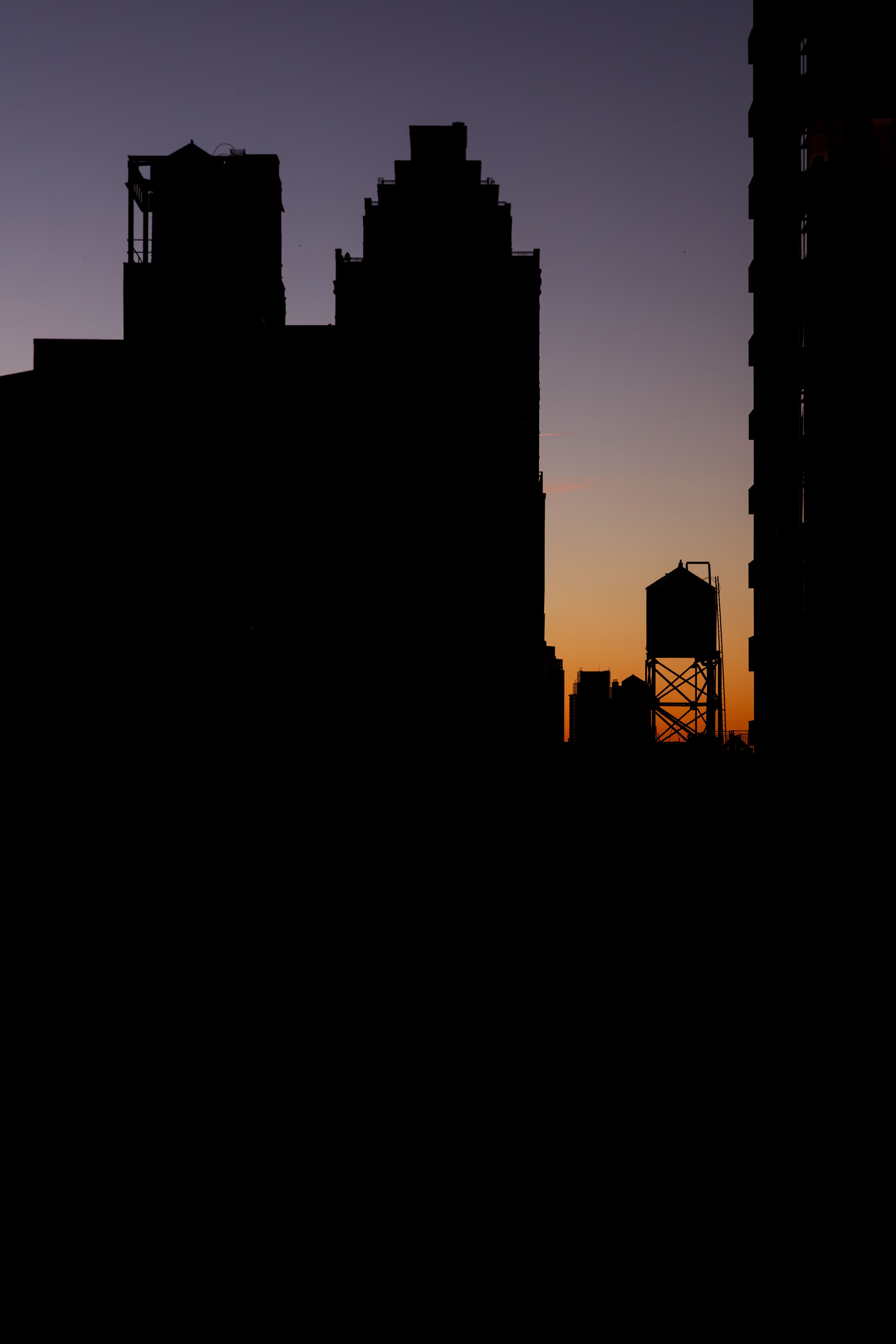 Silhouette of New York City skyline with water tower at sunset.