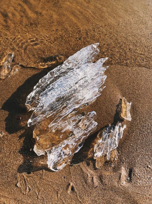 Free Close-up of a clear ice chunk on a sandy beach with water ripples. Stock Photo