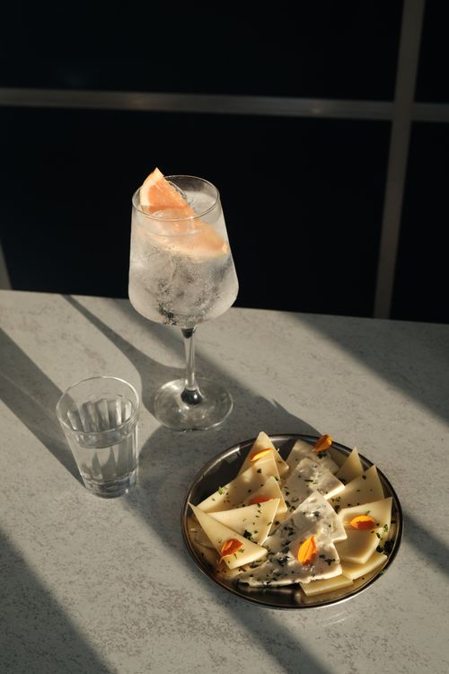 Free Elegant cocktail with grapefruit and cheese platter on a sunlit table. Stock Photo