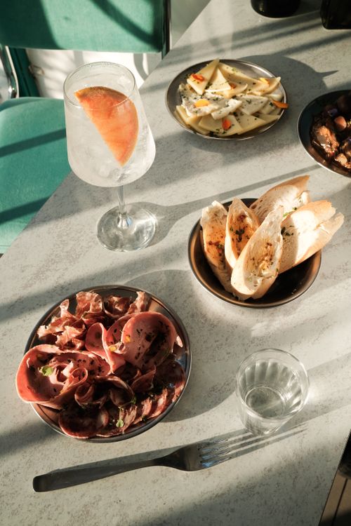 Free Elegant arrangement of prosciutto, cheese, bread, and a refreshing drink on a table. Stock Photo