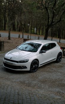 White Volkswagen Scirocco parked in a scenic forest area, showcasing sleek design.