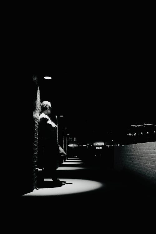 Black and White Photography of a Man Standing under a Streetlight in a City 