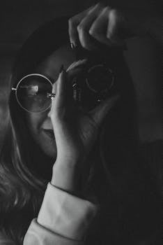 Black and white portrait of a woman with sunglasses capturing a photo.