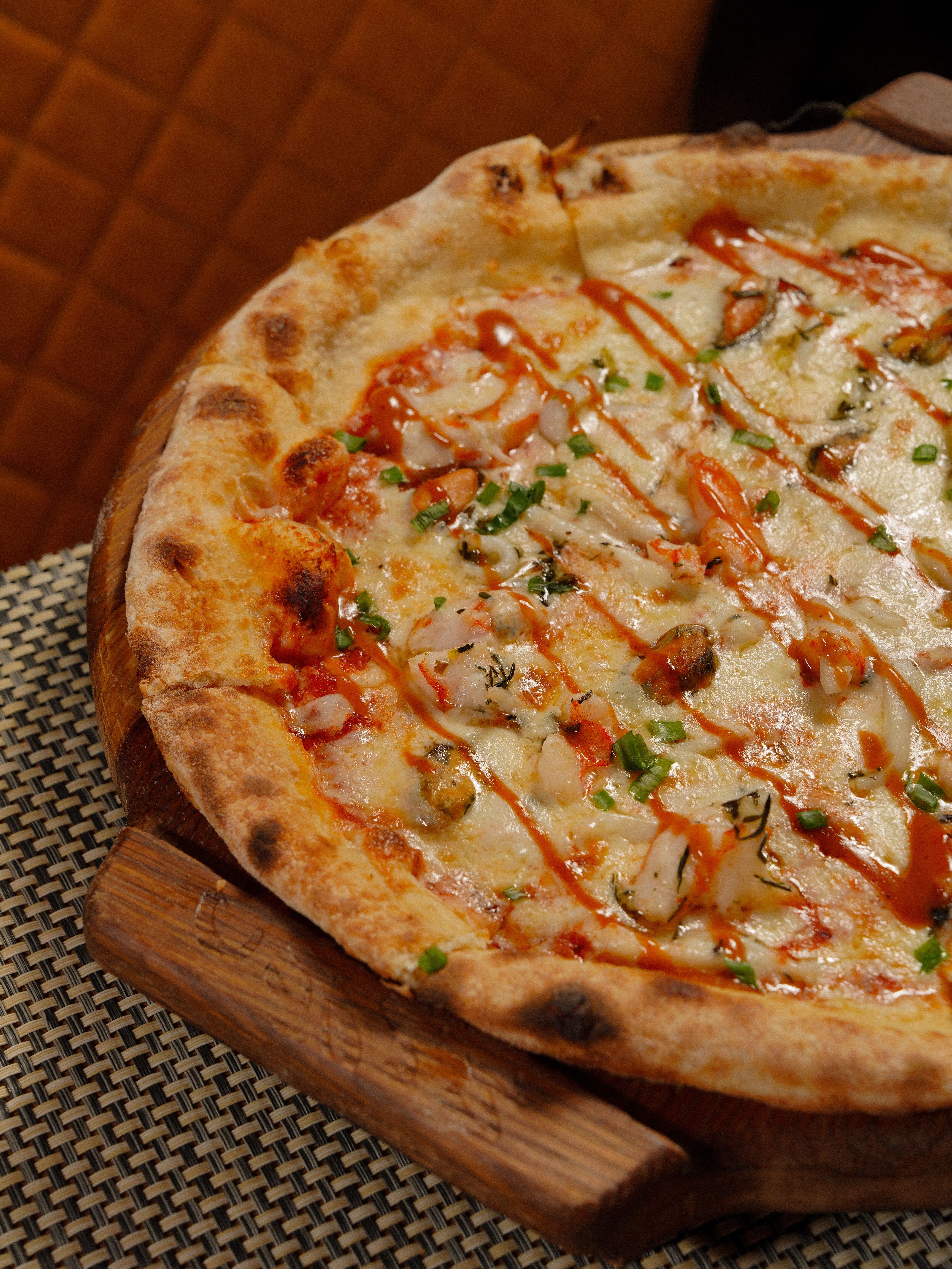 Close-up of a gourmet pizza with cheese, herbs, and drizzle on a wooden board.