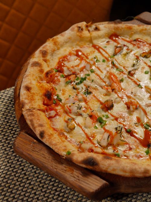Free Close-up of a gourmet pizza with cheese, herbs, and drizzle on a wooden board. Stock Photo