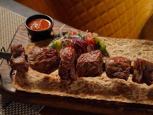 A wooden tray with meat skewers and sauce