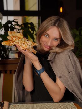 A cheerful woman posing with pizza indoors at a cozy restaurant setting, enjoying a casual meal.