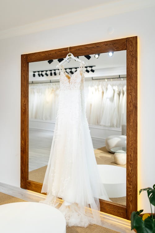 A wedding dress hangs in a mirror in a store