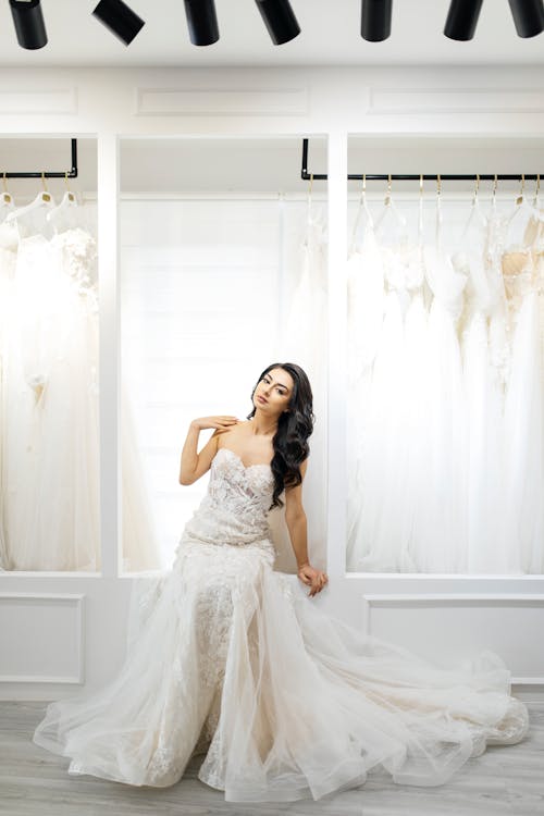 A woman in a wedding dress poses in front of racks of wedding dresses
