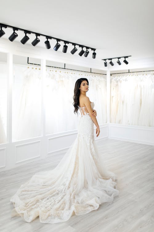 A woman in a wedding dress stands in front of a white wall