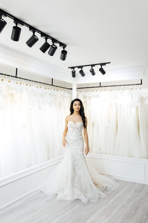 A woman in a wedding dress stands in front of racks of wedding dresses