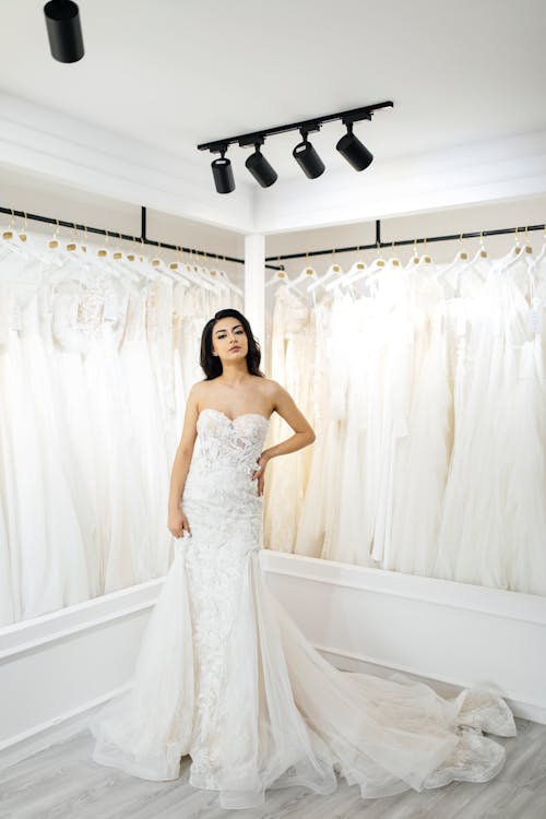 A woman in a wedding dress stands in front of a rack of wedding dresses