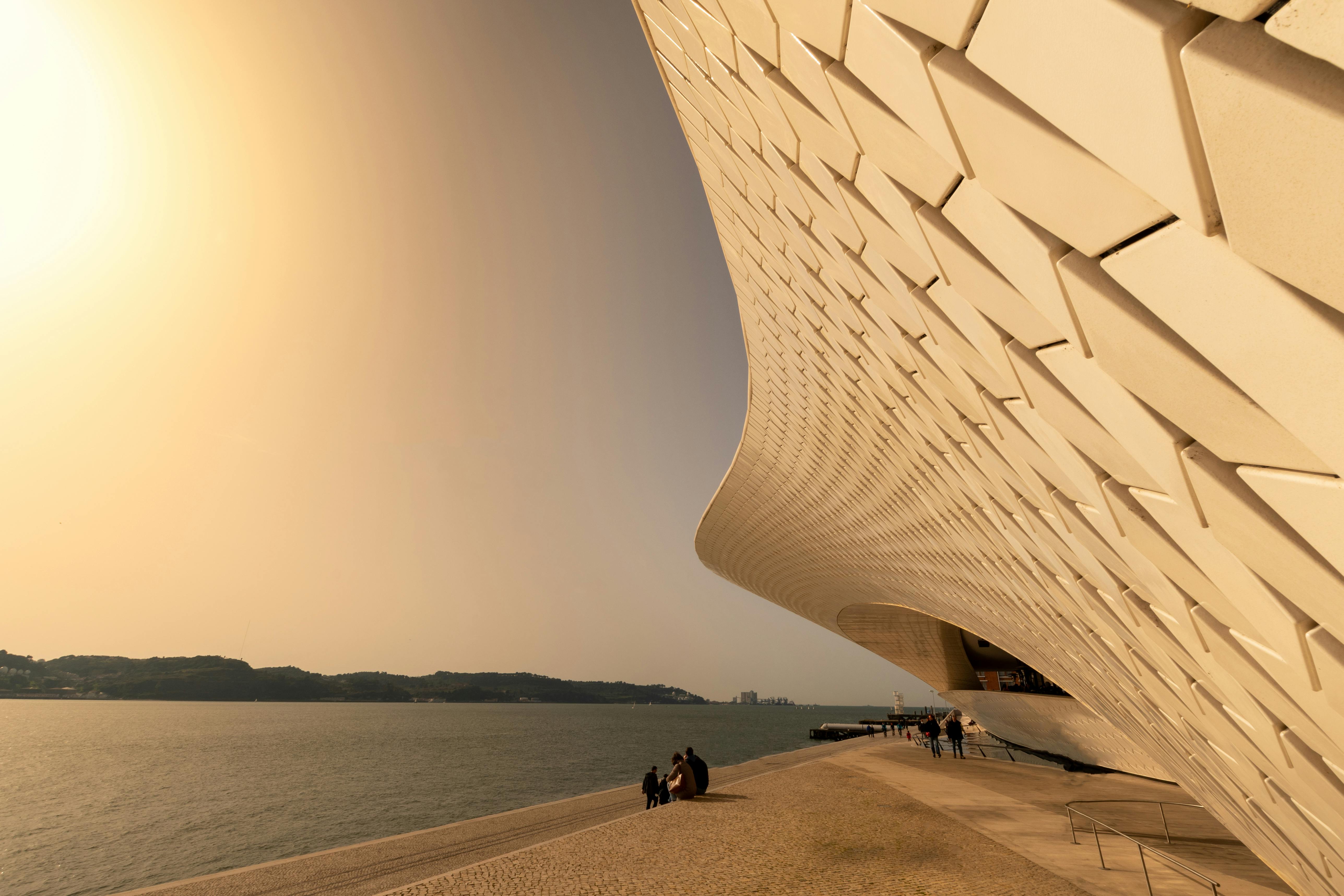 A stunning modern architectural structure by the seaside with people enjoying the summer sunset.