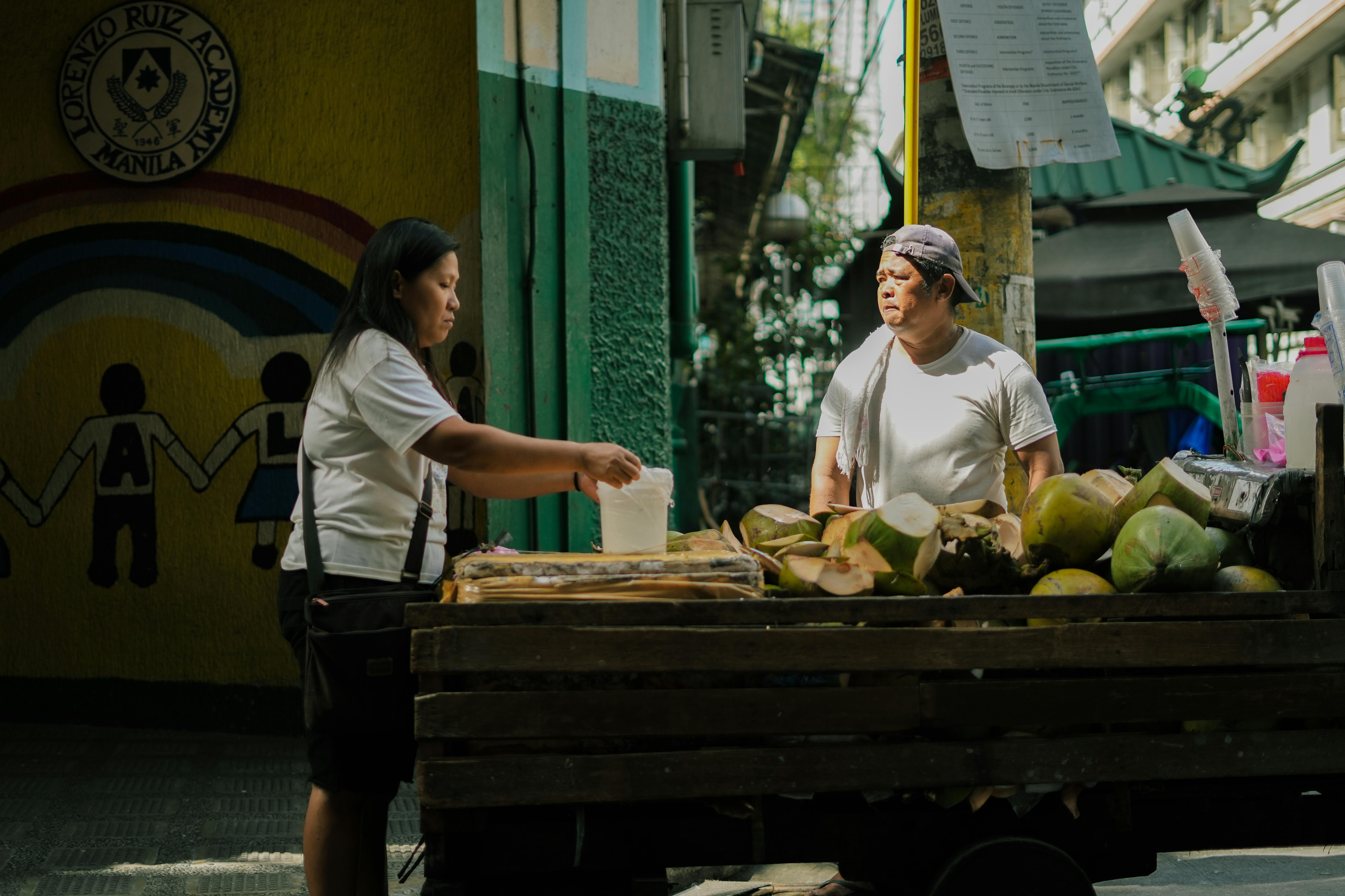 Woman buying fresh coconuts from a street vendor in Manila's urban streets during daytime.