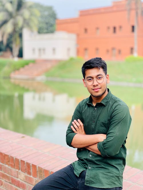 A young man is sitting on a brick wall near a pond