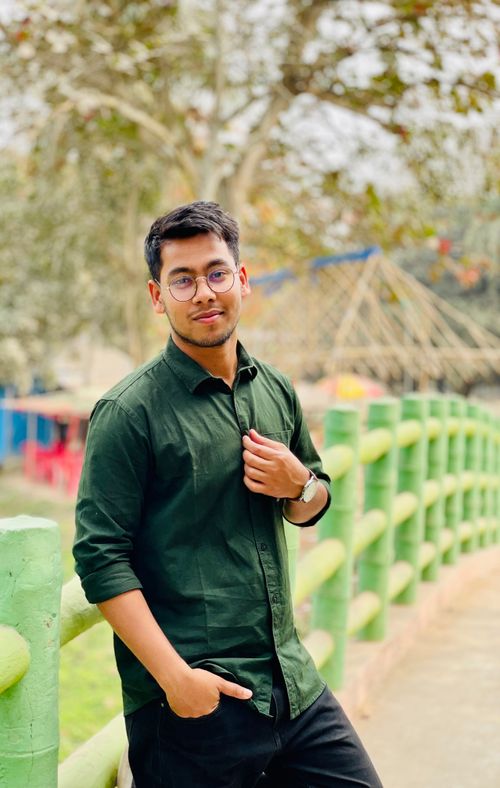 Free Portrait of a fashionable young man outdoors with eyeglasses and short hair, standing confidently on a green bridge. Stock Photo