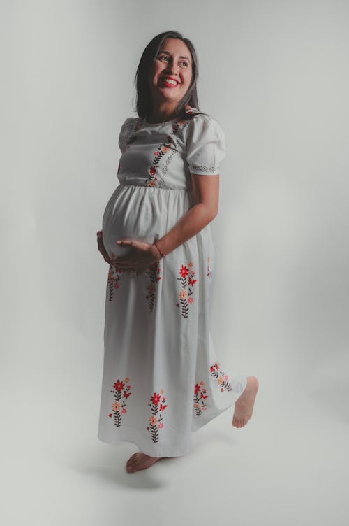 A pregnant woman in a white dress smiling