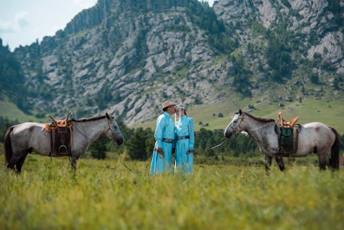 Two people in traditional clothing standing next to horses
