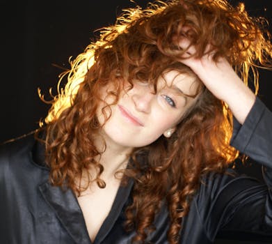 A woman with curly hair and a joyful expression poses against a dark background, capturing a lively mood.