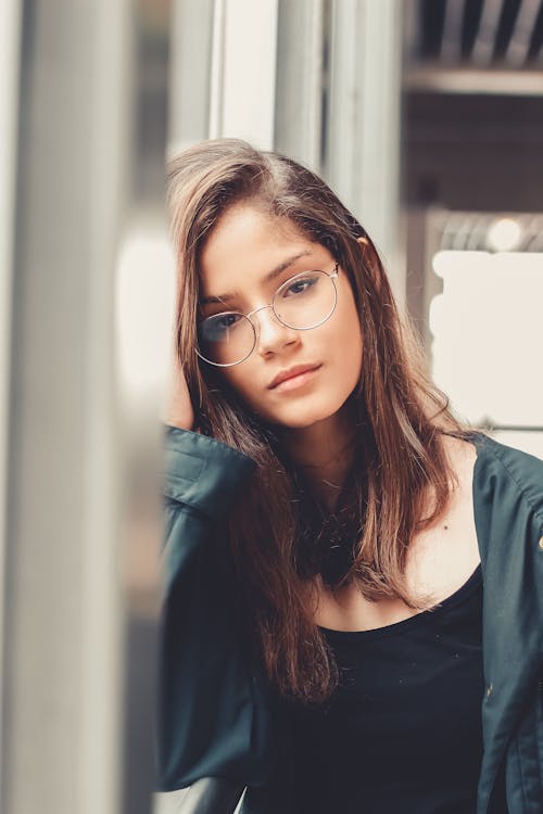 Photo of Woman in Eyeglasses Leaning on Window Sill