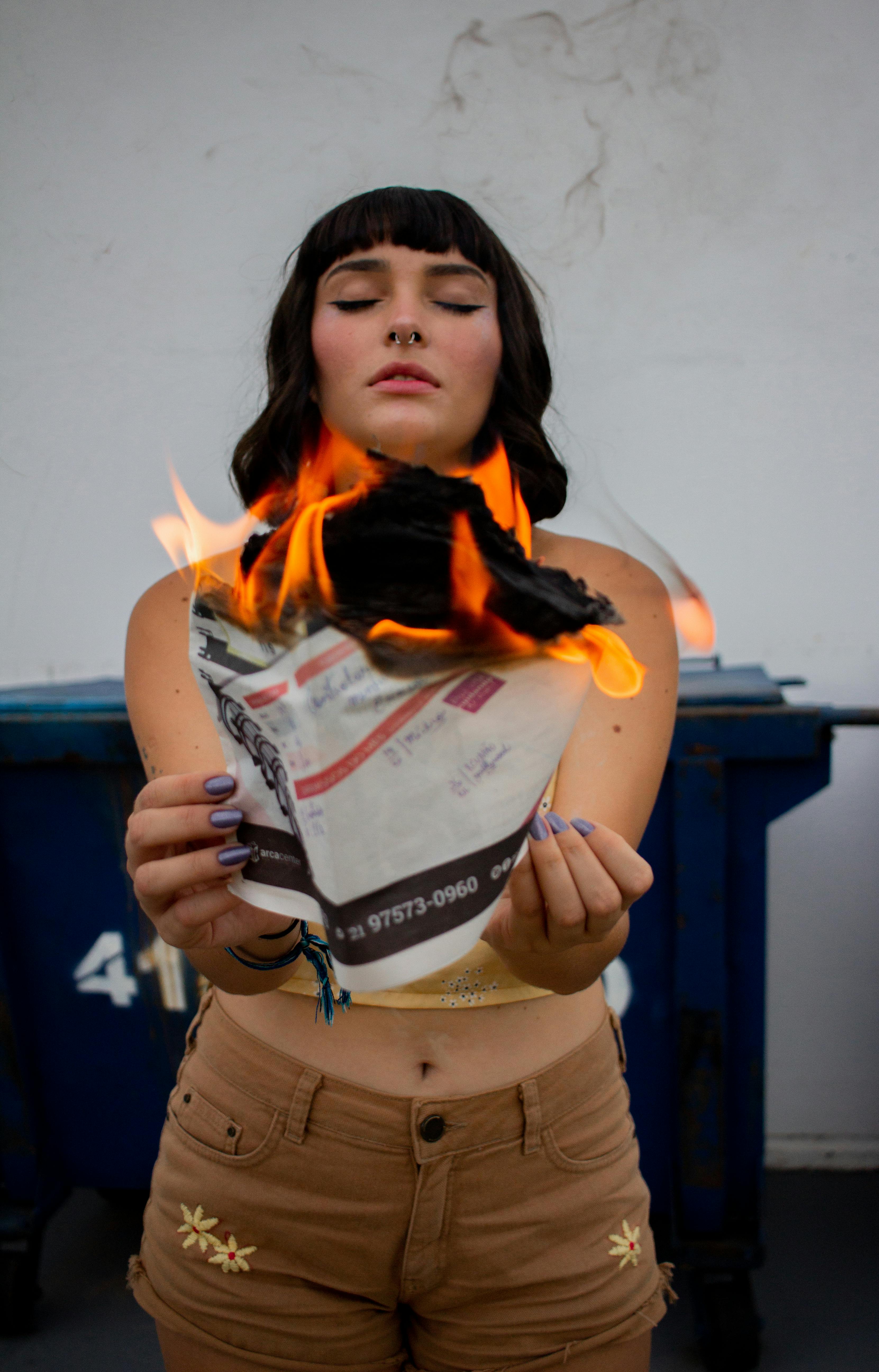 一名年轻女子手持燃烧的报纸，站在户外，营造出戏剧性的场景