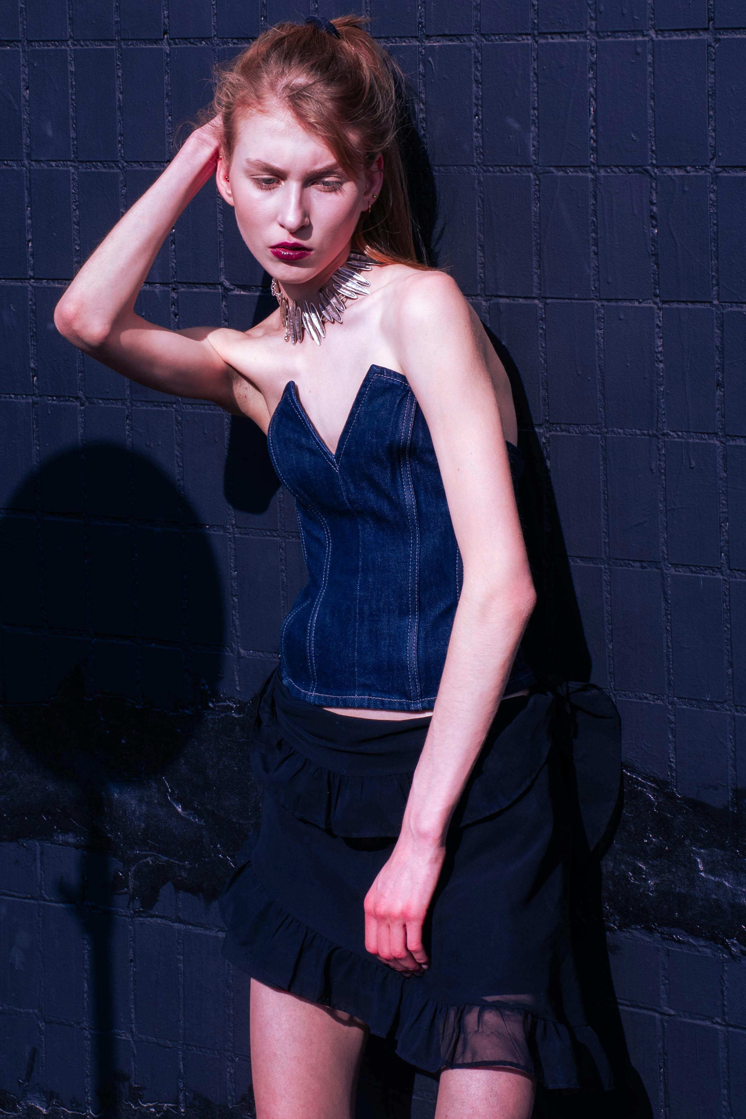 Portrait of a stylish woman in a denim corset striking a pose against a textured wall.