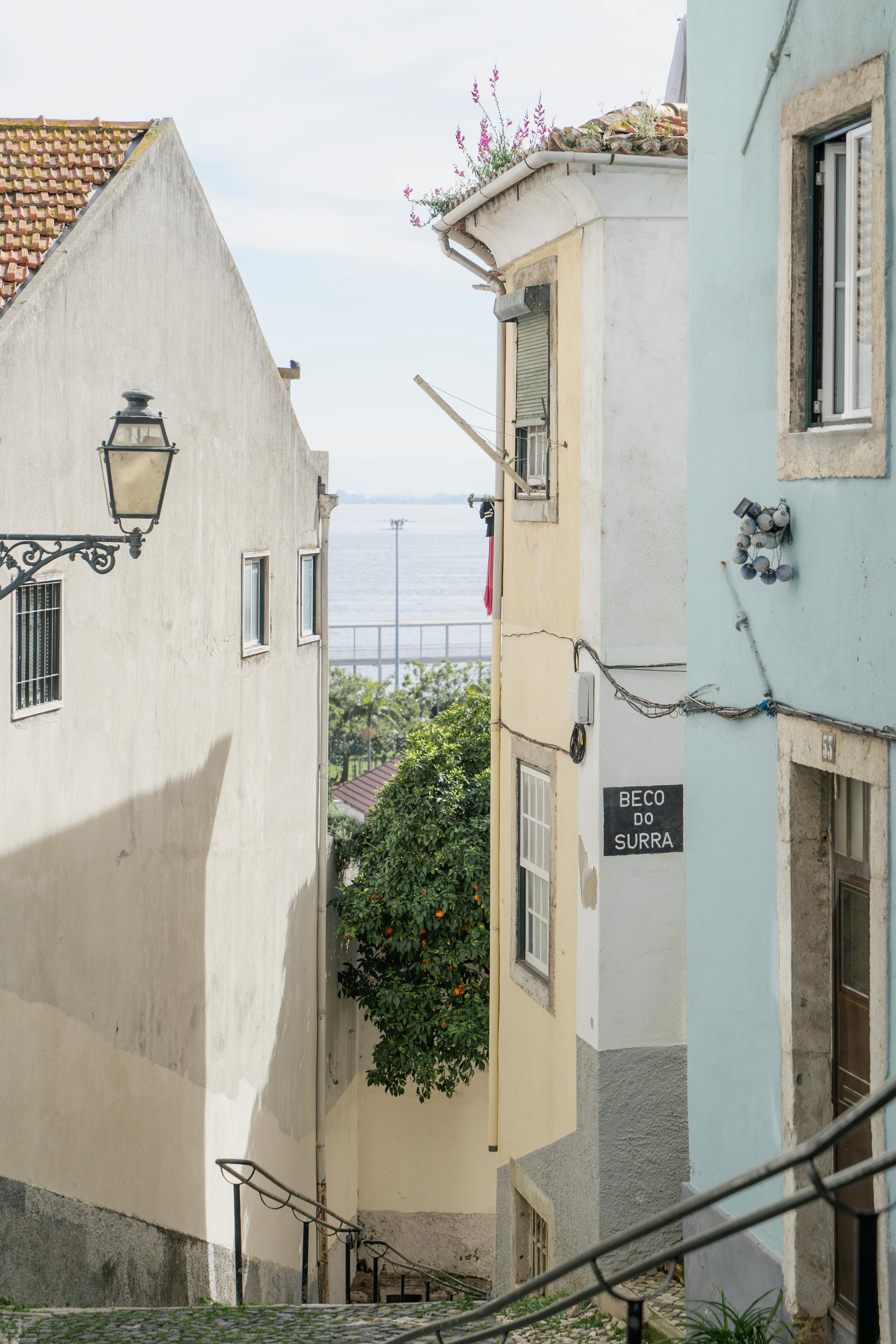 Explore a quaint alleyway in Lisbon, Portugal, featuring pastel buildings and ocean view.
