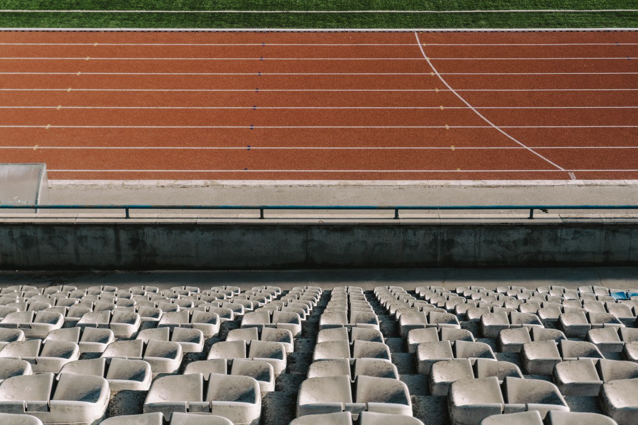rows of empty stadium seats with a view of the running track under day