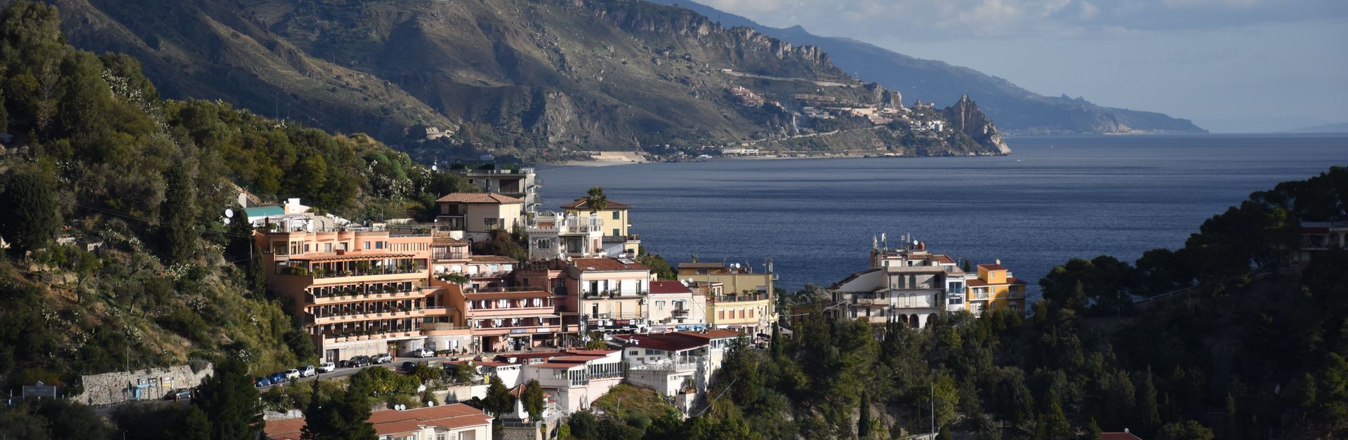 Breathtaking coastal view of Taormina, Sicily, with lush hills and Mediterranean Sea under cloudy sk