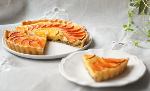 Free A sliced orange tart on a white plate set on a linen tablecloth, highlighting its vibrant citrus design. Stock Photo
