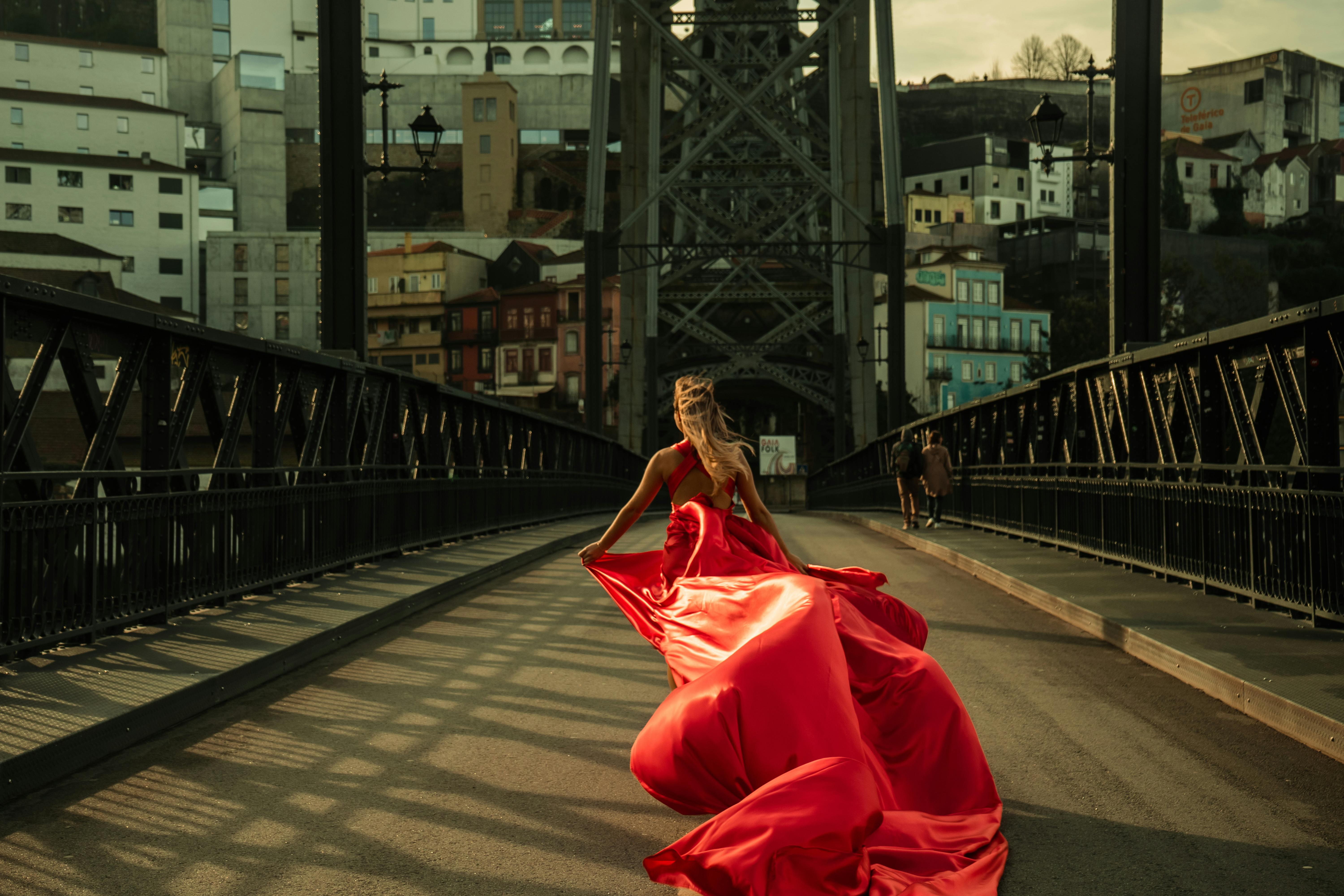 A woman in a flowing red dress walks on a bridge in Porto, Portugal.