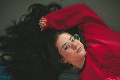 무료 빨간 크루 넥 스웨터를 입은 여자가 바닥에 누워있는 사진 스톡 사진