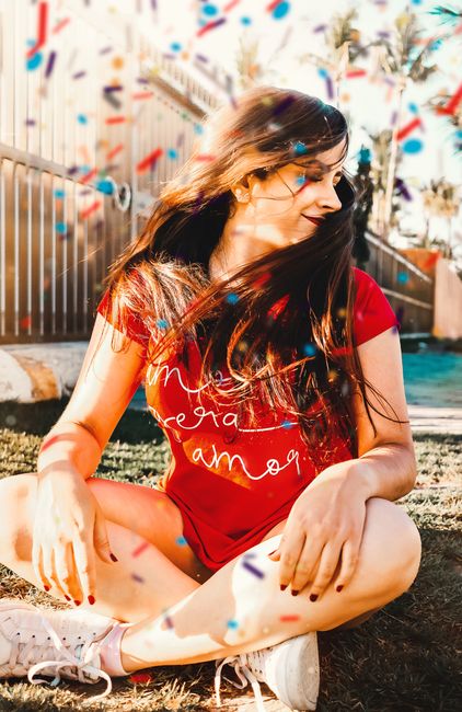 Young woman in red t-shirt enjoying outdoors with colorful confetti around, embodying fun and happiness.