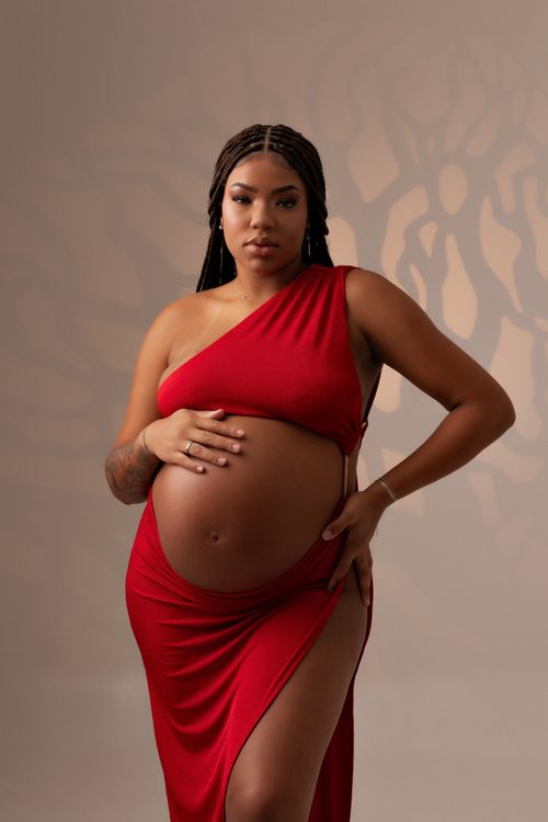 Free Pregnant woman in a braided hair poses elegantly in a red dress during a studio photoshoot. Stock Photo