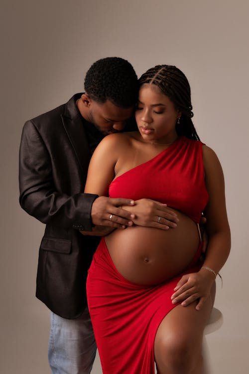 A pregnant woman in a red dress is sitting on a chair