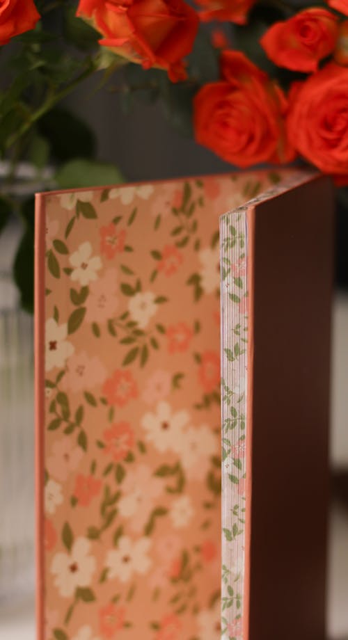 A Notebook with a Floral Pattern Inside Standing next to Flowers 