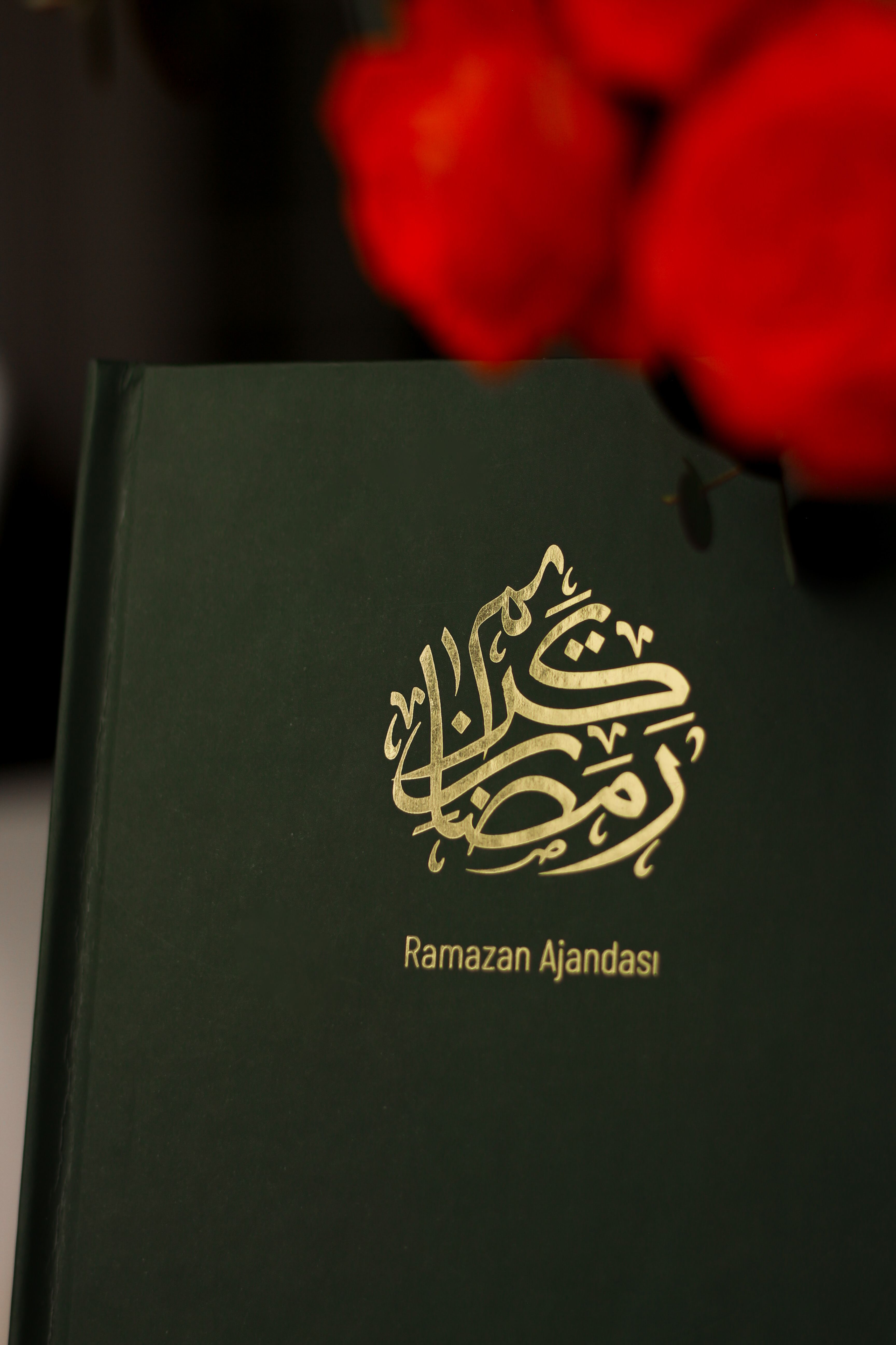 Close-up of a Ramadan planner with gold text and vibrant red flowers in the background.