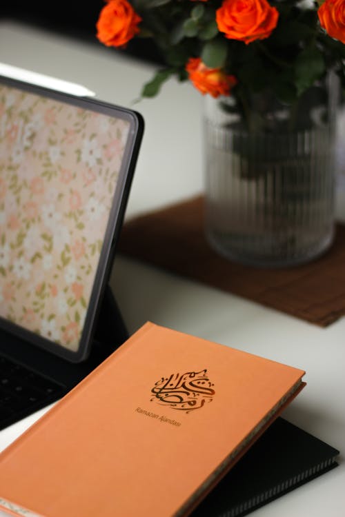 A Calendar Lying next to a Tablet and Flowers in a Vase on a Table 