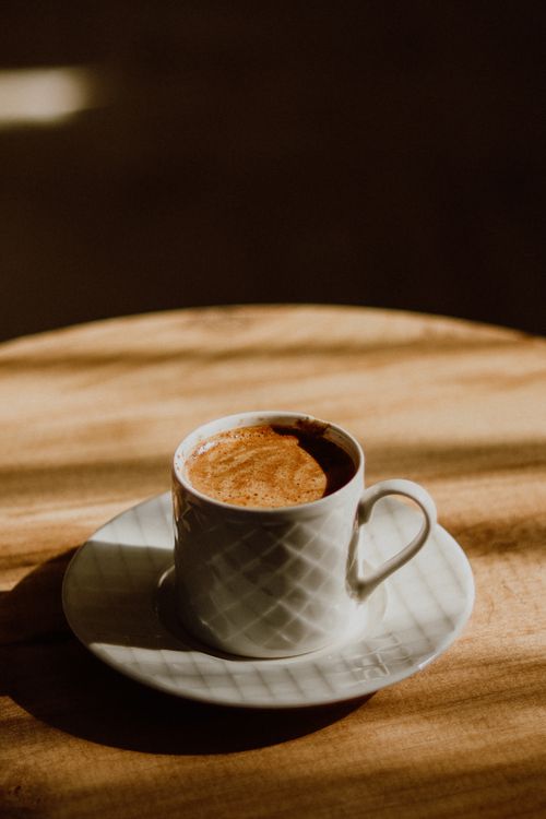 Free A warm espresso shot in a textured white cup casts shadows on a wooden table. Stock Photo
