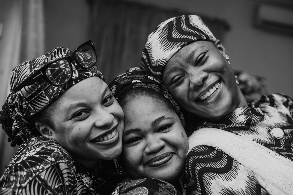 Group of young Black Nigerian friends in a Birmingham living room sorting and dividing shared bags of bulk groceries including rice sacks and palm oil containers into individual piles on the floor, warm evening indoor light, photorealistic