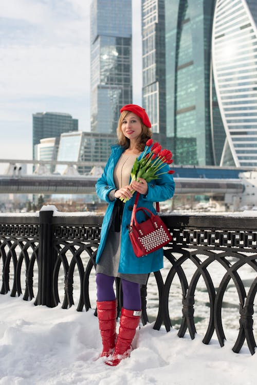 A woman in red boots and a blue coat holding flowers