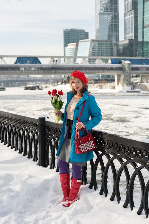 A woman in red boots and a blue coat standing on a bridge with flowers