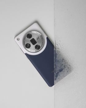 A sleek smartphone featuring a quad camera design resting on a shiny wet surface, showcasing modern technology.